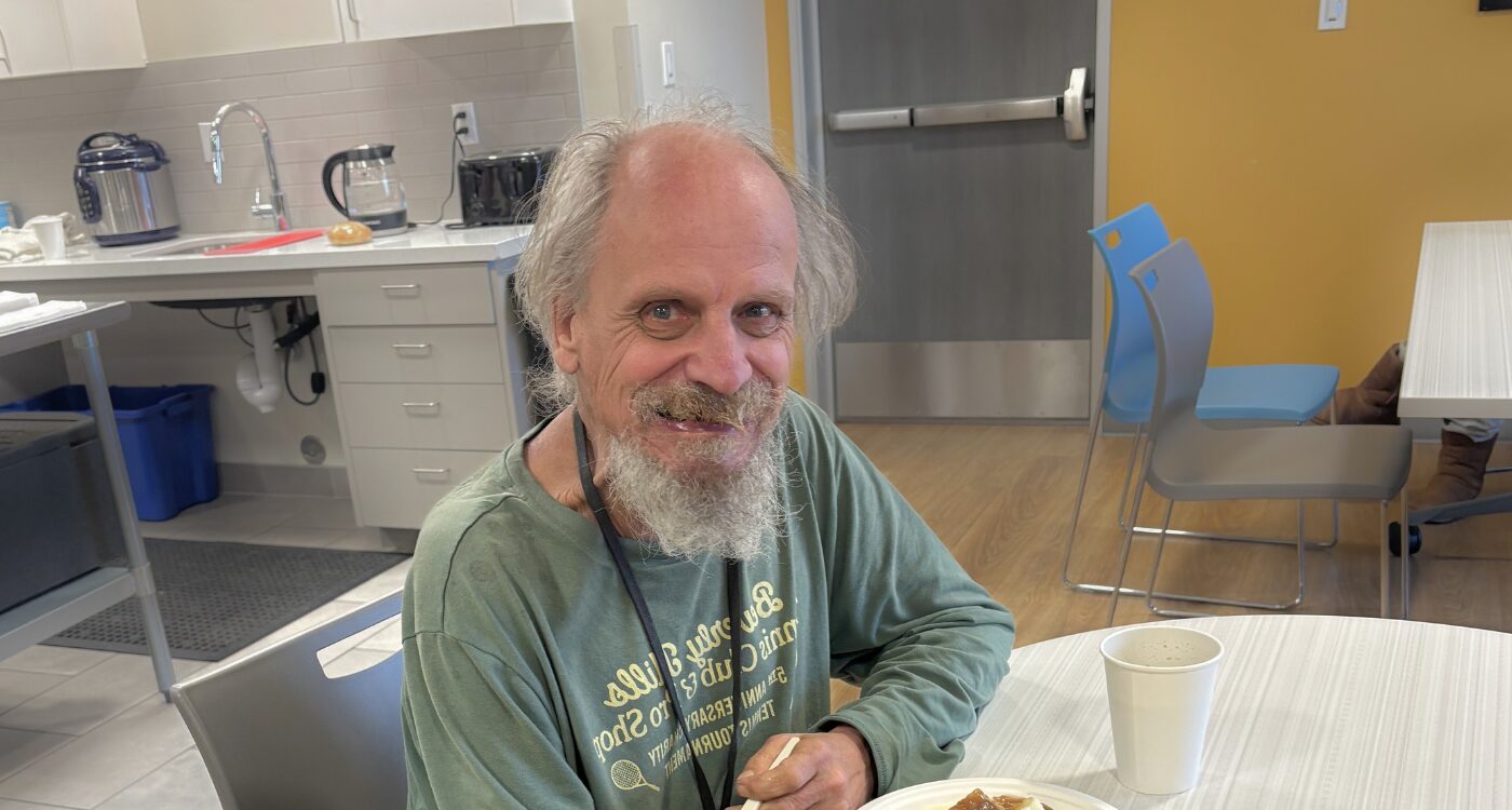 Older man with gray hair and beard sits at dining table