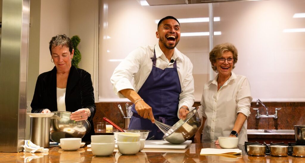 Chef in white coat and blue apron stirs bowl while standing in the showcase kitchen