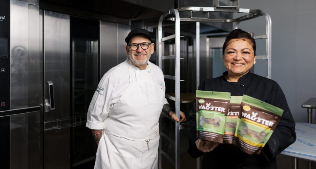 Chef stands by industrial oven next to baker holding bags of Wagster Treats