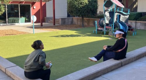 Two women have a chat while sitting near a playground