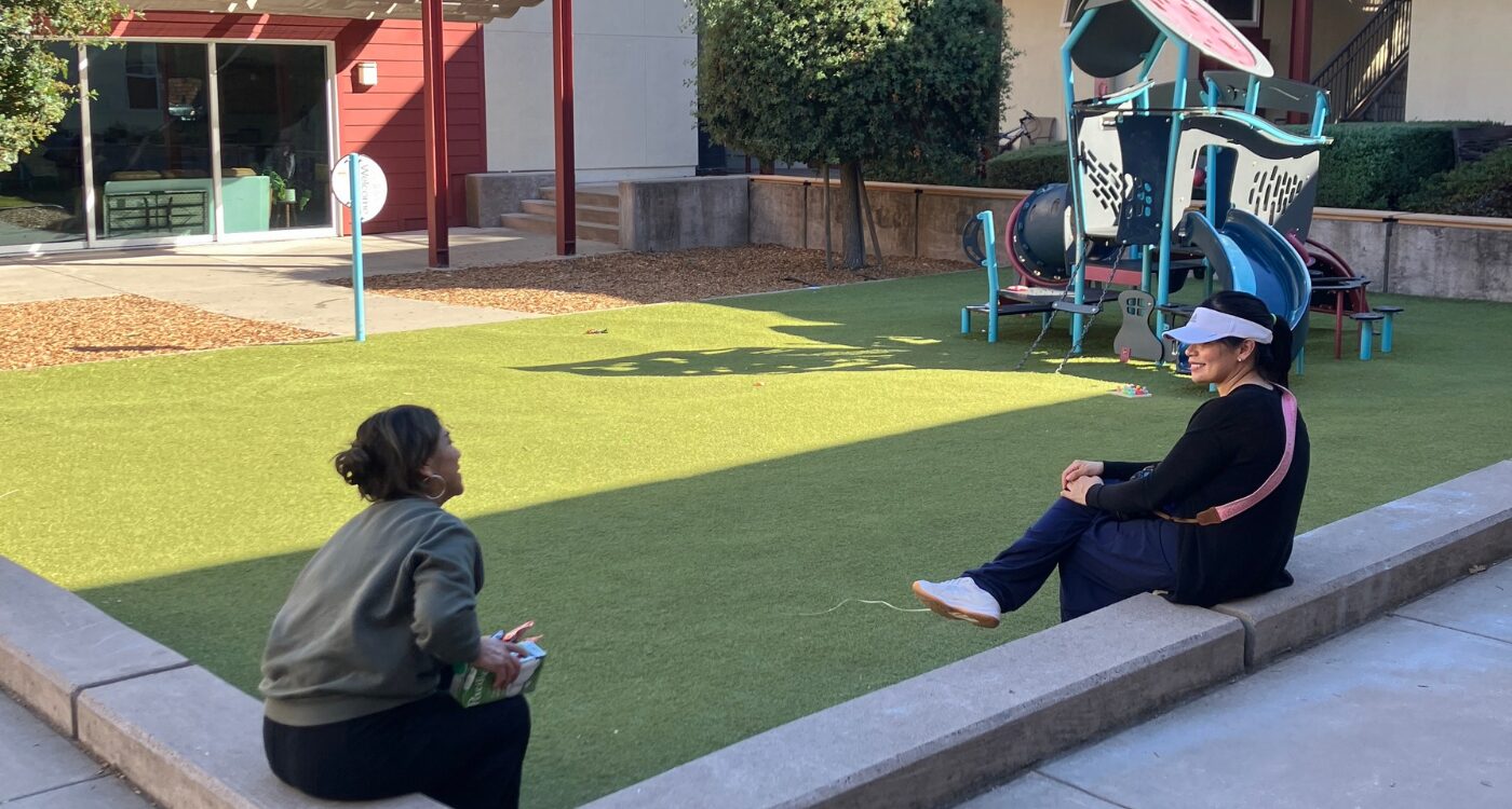 Two women have a chat while sitting near a playground